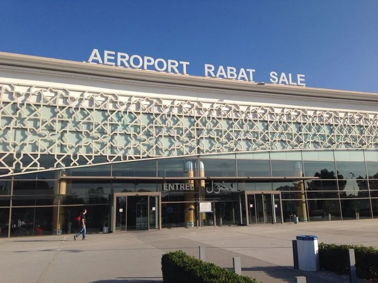 Travelers walking toward the entrance of Rabat–Salé Airport in Morocco with luggage.