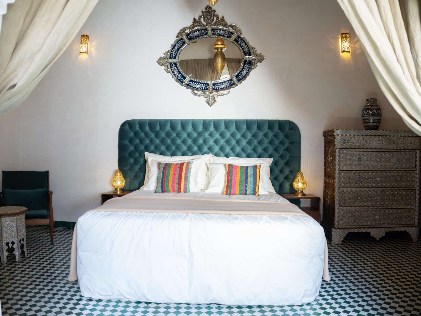 Luxury king bedroom at Riad Dar Flores in Fes featuring a velvet headboard, handcrafted Moroccan mirror, and elegant boutique riad décor.