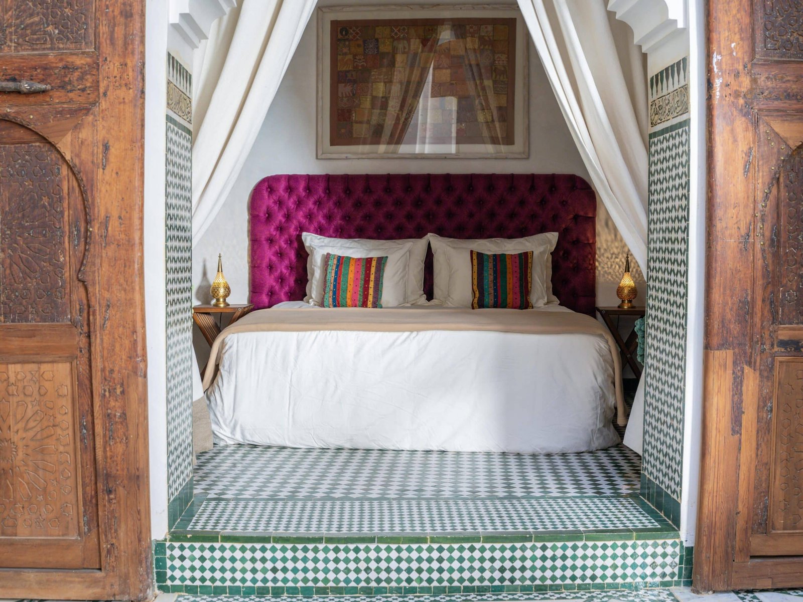Lit king-size dans une suite de riad à Fès avec alcôve, zellige marocain et rideaux blancs.