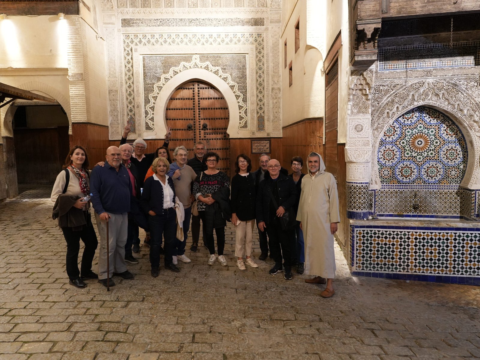 Group of visitors posing in front of a beautifully decorated traditional gate in the historic Medina of Fez, Morocco.