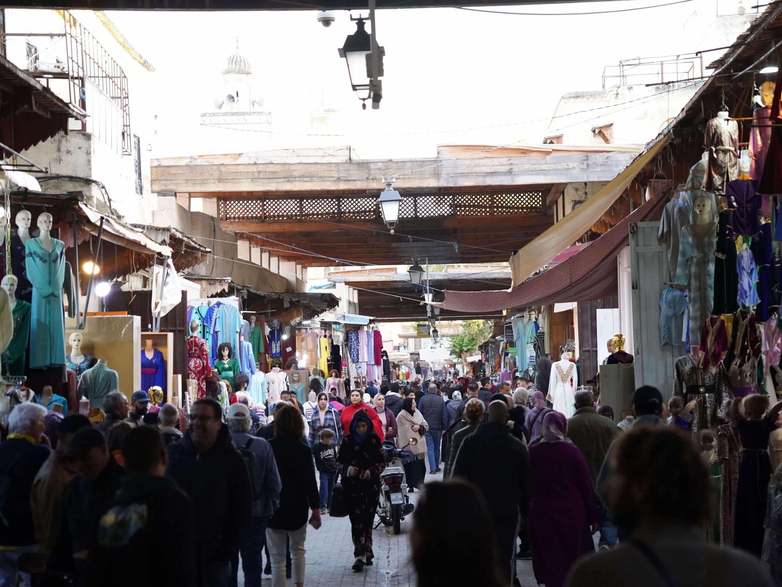 Busy shopping street inside the Medina of Fez with traditional clothing shops and local visitors.